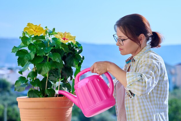 Eine erwachsene Frau, die eine Blume in einem Topf aus einer Gießkanne gießt