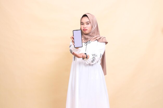 eine erwachsene indonesische muslimische frau, die einen hijab trägt, runzt die stirn und zeigt einen handy-gadget-bildschirm, um c zu erstellen