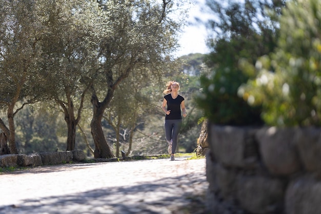 Eine erwachsene lächelnde Fitnessfrau, die im grünen Park joggt