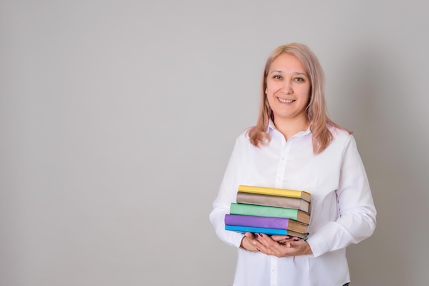 Eine erwachsene Lehrerin hält einen Stapel Bücher in ihren Händen, die auf einem grauen Hintergrund stehen, Exemplar