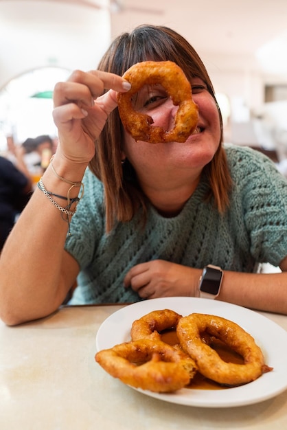 Foto eine europäerin isst zum nachtisch einen teller mit peruanischen picarones und spielt mit einem davon, um ihn durchzusehen