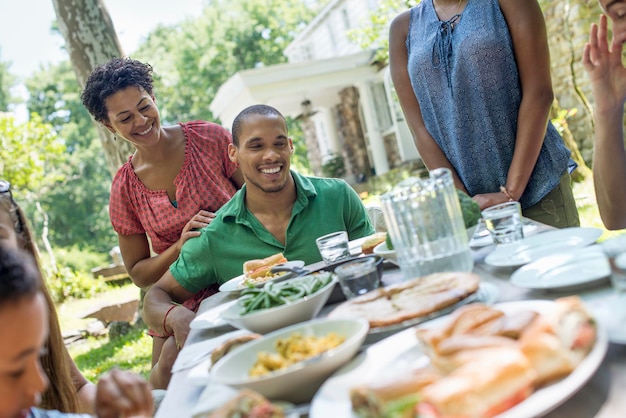 Eine Familie, die im Sommer Männer, Frauen und Kinder um einen Tisch in einem Garten versammelt