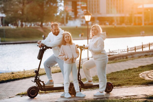 Eine Familie in weißer Kleidung steht bei Sonnenuntergang auf Elektrorollern in der Stadt.