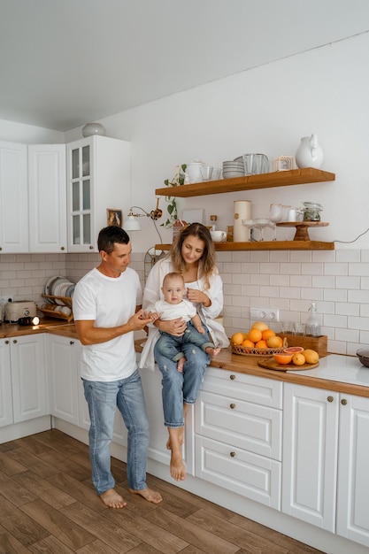 Eine Familie mit einem Baby in Jeans und weißen T-Shirts spielt in der Küche