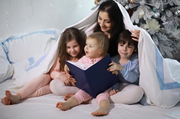 Eine Familie mit Kindern, die sich in den Weihnachtsferien auf dem Bett unter der Bettdecke vergnügt.