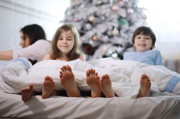 Eine Familie mit Kindern, die sich in den Weihnachtsferien auf dem Bett unter der Bettdecke vergnügt