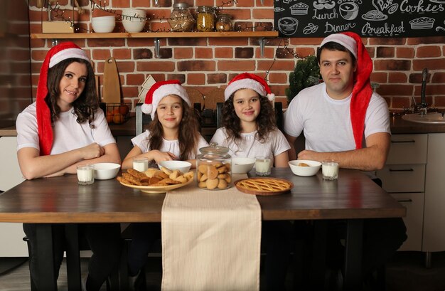 Eine Familie mit Weihnachtsmannmützen sitzt in der Küche auf dem Tisch mit Milch und Keksen