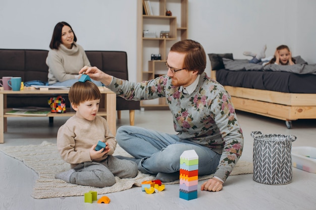 Eine Familie mit zwei Kindern, die zusammen auf dem Boden spielen und zu Hause Spaß haben.