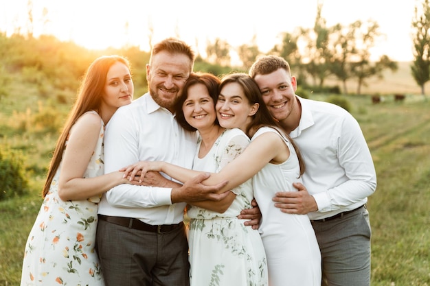 Eine Familie unterschiedlichen Alters umarmt sich bei Sonnenuntergang fest in der Natur. Familie mit fünf Personen glücklich zusammen. Porträt einer Familie mittleren Alters. eine gruppe von Menschen