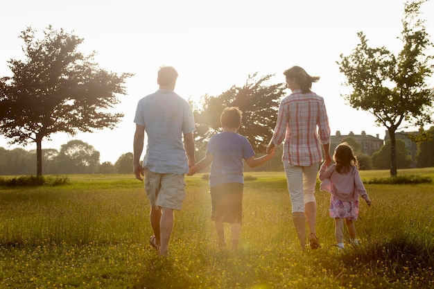 Eine Familie, zwei Eltern und zwei Kinder, die im Sommer Hand in Hand über Gras im Freien laufen