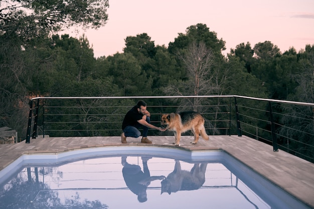 Eine faszinierende Aufnahme eines jungen Mannes, der mit einem deutschen Schäferhund nahe dem Schwimmbad spielt