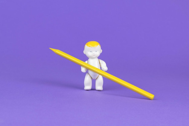Eine Figur eines Babys, das einen großen gelben Bleistift auf violettem Hintergrund hält.