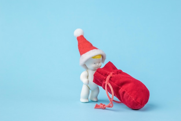 Eine Figur eines Babys in einer roten Mütze, das in eine Tasche mit Geschenken schaut. Das Konzept des neuen Jahres.