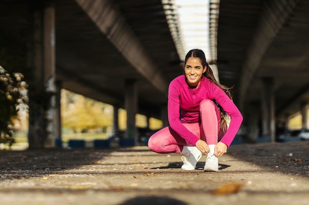 Eine fitte Sportlerin, die sich im städtischen Äußeren hockt und Schnürsenkel bindet