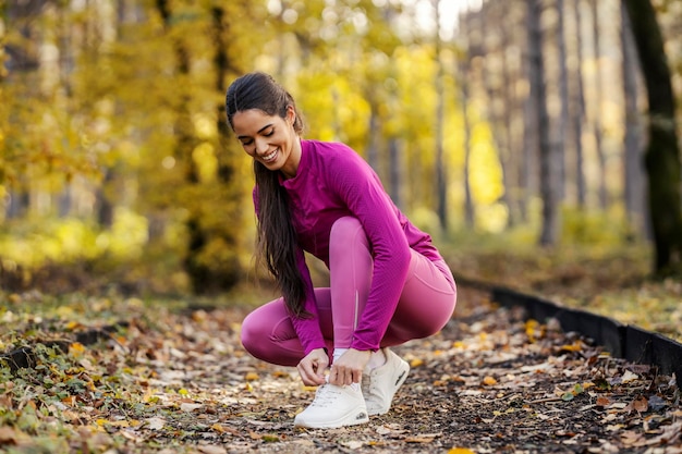 Eine fitte Sportlerin sitzt in der Natur und tippt ihre Schnürsenkel, während sie sich auf das Training vorbereitet