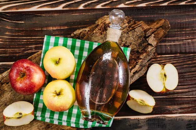 Foto eine flasche apfelessig und rohe frische äpfel auf holzhintergrund