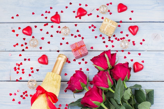 eine Flasche Champagner, ein Strauß roter Rosen und zwei Geschenke in einer Schachtel
