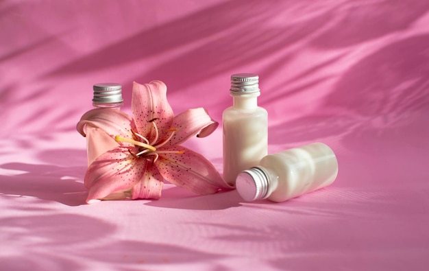 Eine Flasche Creme, Lotion, Mousse, Reiniger, Shampoo zur Haut- und Haarpflege. Weiße Plastikverpackungen in Folge auf einem leuchtend rosa Hintergrund, verziert mit Blumenschatten. Layout von Salonprodukten.