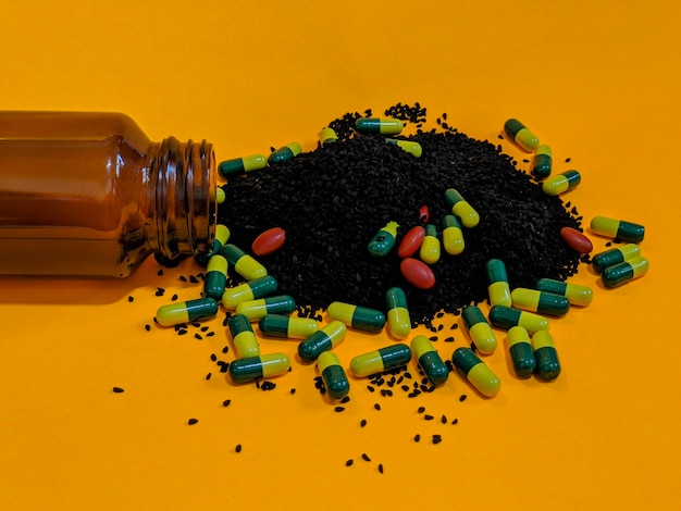 Eine Flasche grüne gelbe Pillen und schwarze Samen auf orangefarbenem Hintergrund