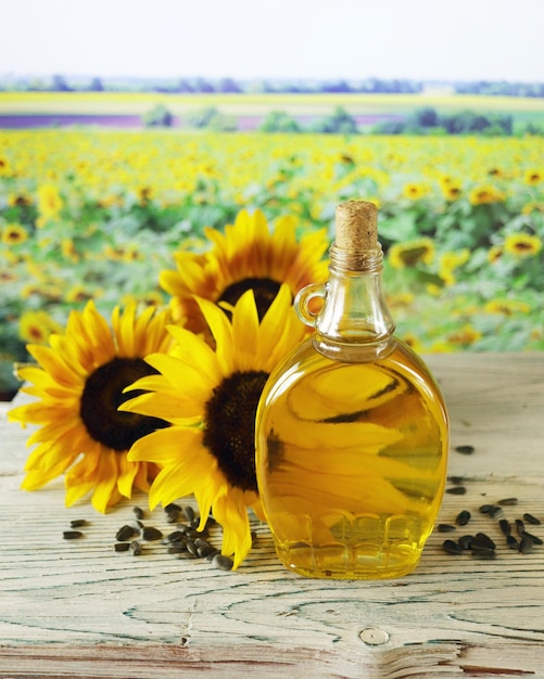 Eine Flasche Öl, frische Sonnenblumenblüten und Samen auf dem Tisch, eine Landschaft mit blühendem Feld