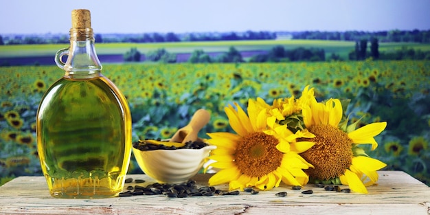 Eine Flasche Öl, frische Sonnenblumenblüten und Samen vor dem Hintergrund einer Landschaft