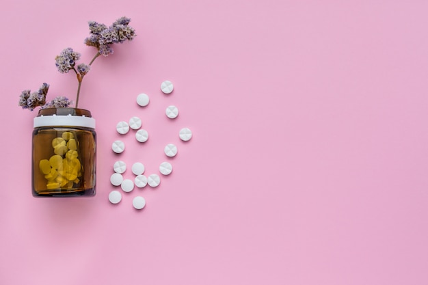 Eine Flasche Medikamente und verstreute Pillen auf einem pastellrosa Hintergrund. Zerrissene Vitamine auf hellem Hintergrund. Heilkräuter.