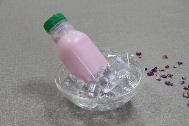 Eine Flasche Milch mit Rosensirup und Basilikumsamen, serviert in der Seitenansicht einer Eiswürfelschale auf grauem Hintergrund