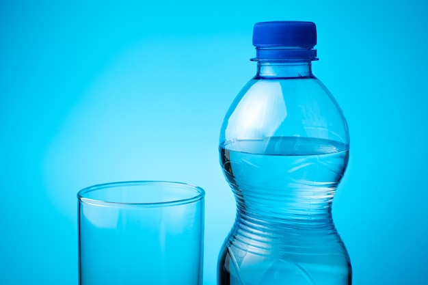 Eine Flasche Mineralwasser und ein leeres Glas auf blauem Grund.