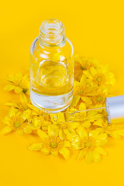 Eine Flasche mit einem Pipettenserum auf gelbem Hintergrund, umgeben von Frühlingsblumen