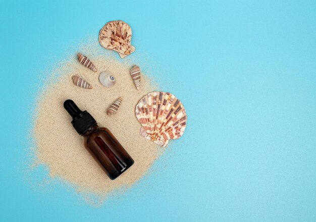 Eine Flasche mit einer Pipette, gefüllt mit Essenz Kosmetiköl Blauer Hintergrund mit Sand und Muscheln Das Konzept der Schönheit und Gesundheit Bio-Kosmetik parfümiert Aromatherapie