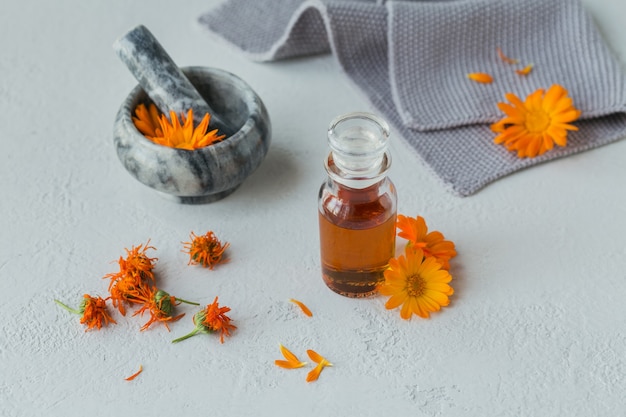 Eine Flasche Ringelblumentinktur oder Aufguss mit frischen und trockenen Ringelblumenblüten auf Weiß