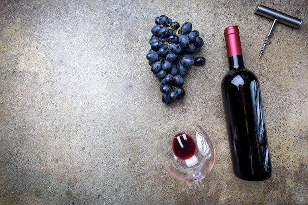 Eine Flasche Rotwein mit Glas und Trauben auf einem grauen Stein