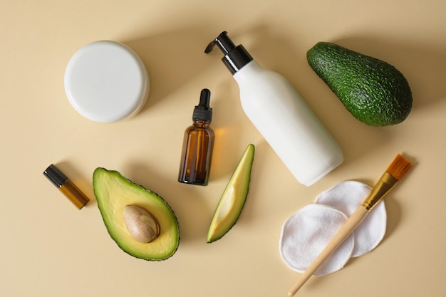 Eine Flasche Sahne mit Spender und Avocadoscheiben auf beigem Hintergrund Naturkosmetik-Konzept Draufsicht