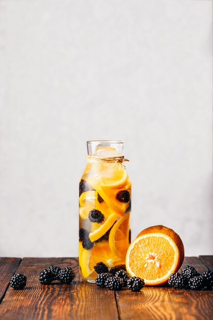 Eine Flasche Wasser mit geschnittener roher Orange und frischer Brombeere. Zutaten auf Holztisch.
