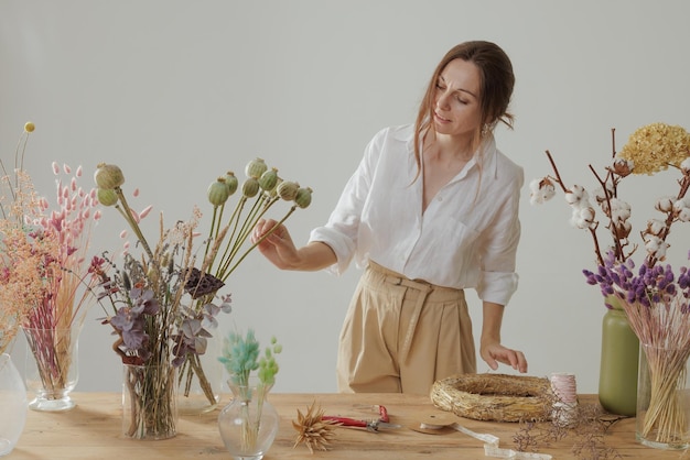 Eine Floristin fertigt in ihrer Werkstatt an einem Holztisch einen unvergänglichen Strauß trockener Blumen an