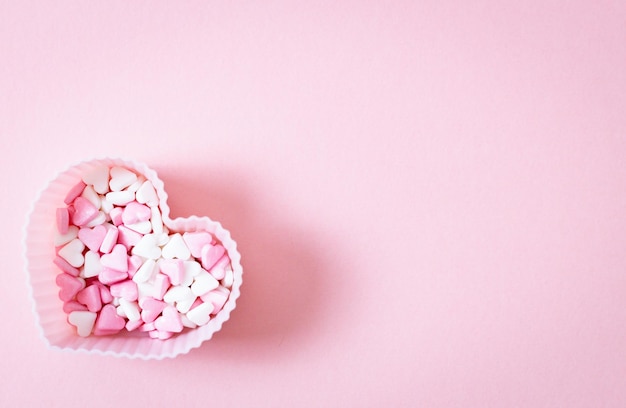 Eine Form für ein Muffinherz mit Zuckerstreuseln auf rosa Hintergrund