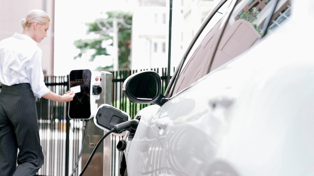 Foto eine fortschrittliche geschäftsfrau installiert den ladestecker von der ladestation in ihr elektroauto, bevor sie durch die innenstadt fährt. umweltfreundliches, wiederaufladbares auto, das mit nachhaltiger und sauberer energie betrieben wird