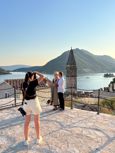 Eine Fotografin fotografiert einen Mann und eine Frau auf einer Aussichtsplattform in der Nähe der St.-Nikolaus-Perast-Kirche