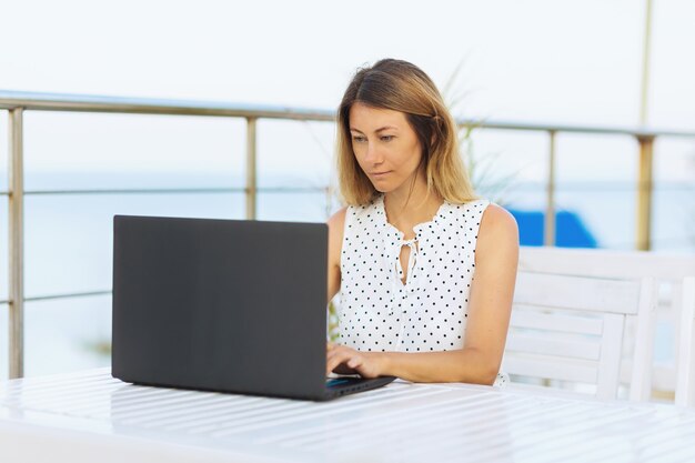 Eine Frau arbeitet in einem Sommercafé am Wasser aus der Ferne an einem Laptop