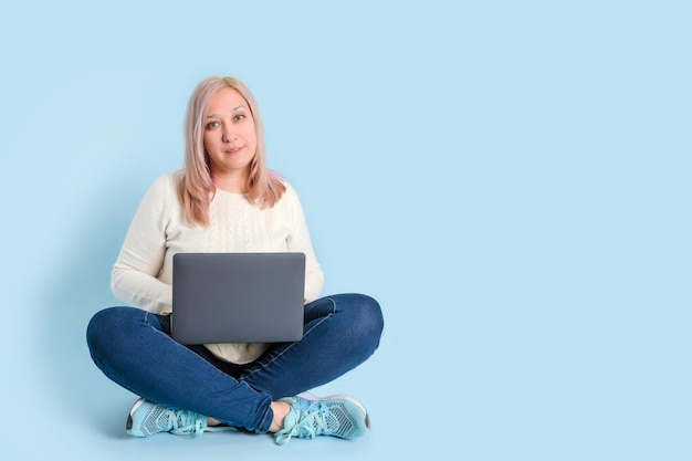 Eine Frau arbeitet mit einem Laptop auf ihrem Schoß, der auf einem blauen Hintergrund sitzt. Kopierbereich