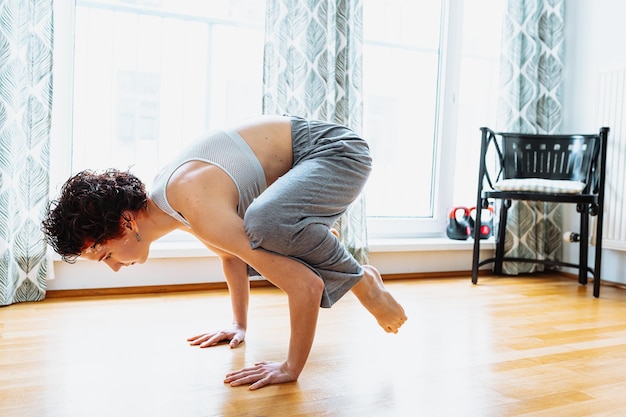 Eine Frau beim Yoga in einem Raum mit einem Fenster hinter ihr.