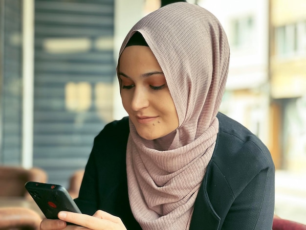 Eine Frau benutzt ein Telefon und sie trägt einen rosa Hijab.