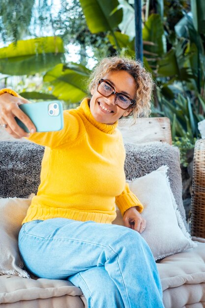 Eine Frau benutzt ihr Handy und entspannt sich allein im Garten, sitzend auf einem Sofa Porträt einer fröhlichen Frau, die auf dem Handy schreibt, eine Dame, die ein Selfie macht, reife junge Leute, die sich entspannen