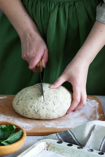 Eine Frau bereitet Brötchen aus Hefeteig mit Brennnesseln zu. Rustikaler Stil.