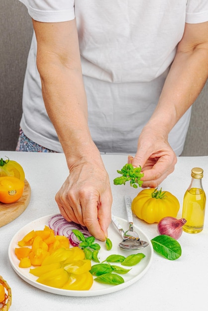 Eine Frau bereitet einen Tomatensalat zu. Reifes Gemüse, Kräuter, aromatische Gewürze, Olivenöl. Hausmannskost mit frischen Zutaten