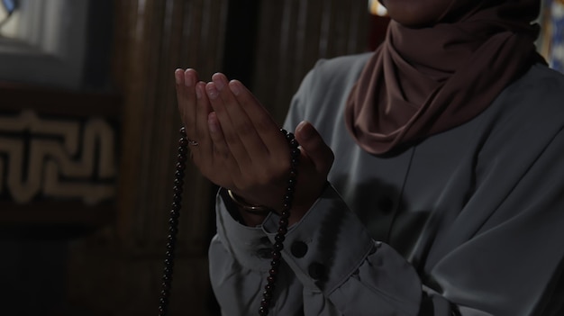 Eine Frau betet in einem dunklen Raum mit einem Rosenkranz in der Hand.