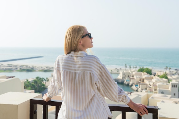 Eine Frau blickt vom Balkon ihres Hotelzimmers aufs Meer