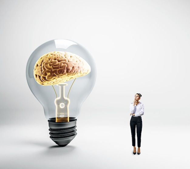 Eine Frau denkt neben einer riesigen Glühbirne mit einem Gehirn im Inneren, das ein Konzept innovativer Ideen und intelligenter Lösungen darstellt