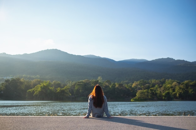 Eine Frau, die allein am See sitzt und die Berge mit grünem Naturhintergrund betrachtet