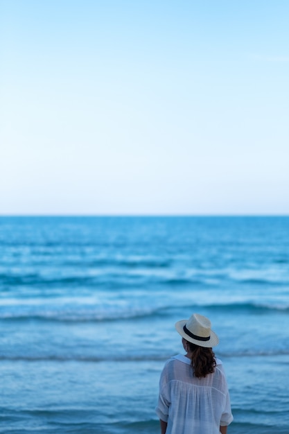 Eine Frau, die am Strand steht und allein auf ein wunderschönes Meer und einen blauen Himmel blickt